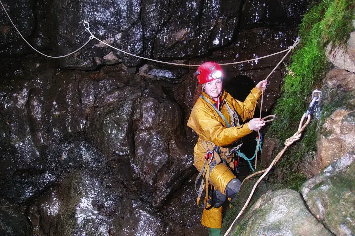 Exploradora en cueva húmeda, usando equipo de seguridad y varios tipos de cuerdas para ascender.