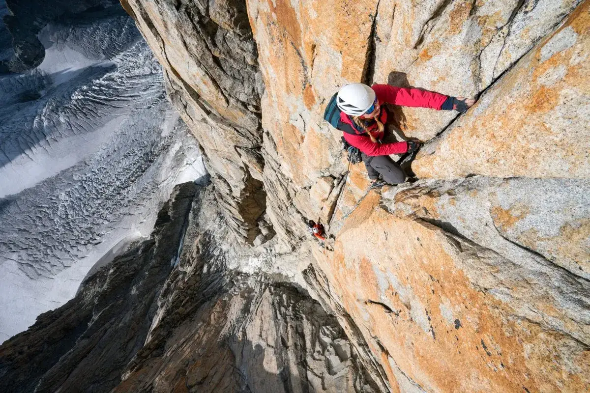 Silvia Vidal escala una pared de roca anaranjada, con un glaciar a la izquierda.