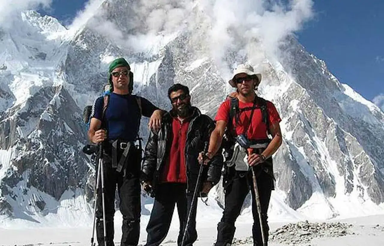 Oscar Pérez alpinista y dos compañeros posan con bastones de trekking ante un imponente pico nevado.
