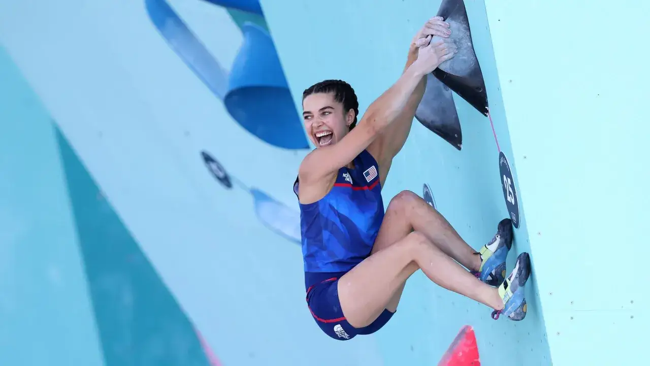 Brooke Raboutou, escaladora estadounidense, sonr&iacute;e mientras se aferra a una pared de escalada azul.