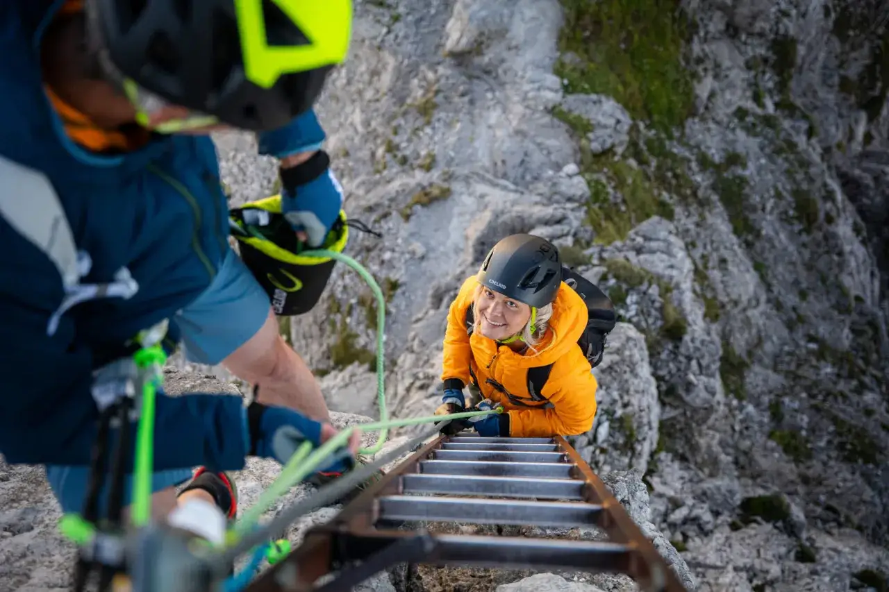 Dos escaladores en una vía ferrata, uno asegurando al otro. El autoseguro es clave en esta emocionante escalada.