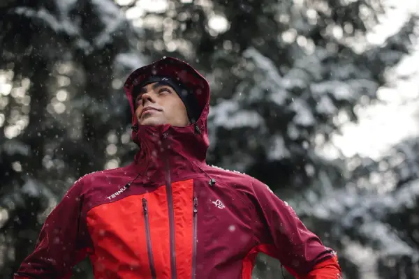 Hombre con ropa para ir a la montaña, con capucha y chaqueta impermeable, bajo una nevada.