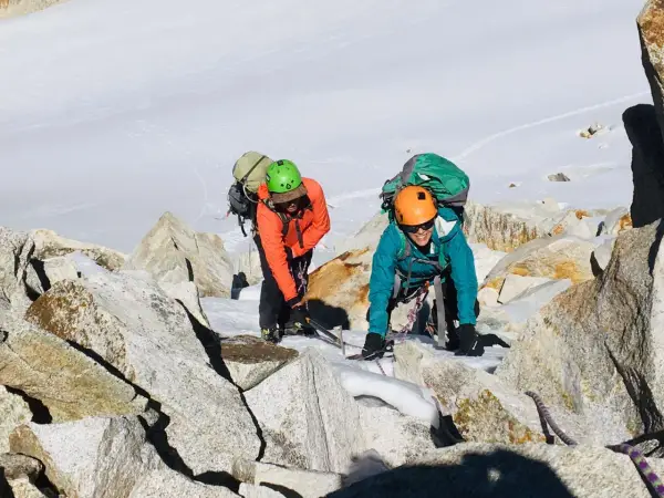 Dos escaladores con mochilas y cascos navegan por rocas y nieve en la montaña. Sus aventuras son como libros abiertos de la naturaleza.
